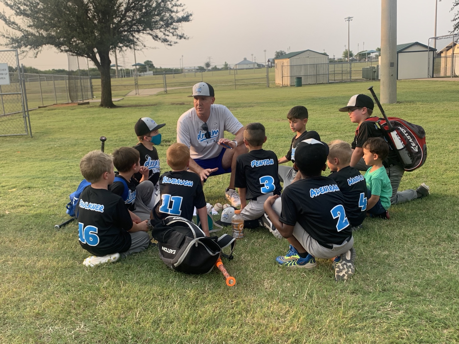 Patrick talking with a circle of young DREAM Team baseball players on the grass