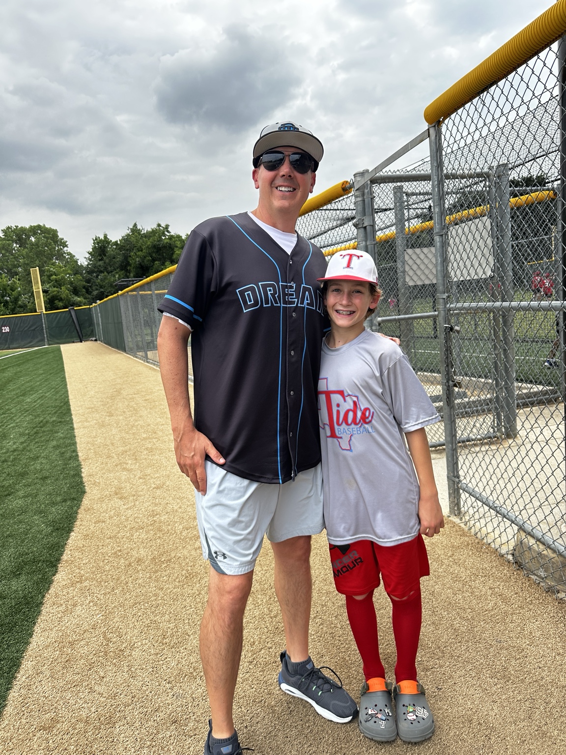 Patrick standing beside a young baseball player next to the field